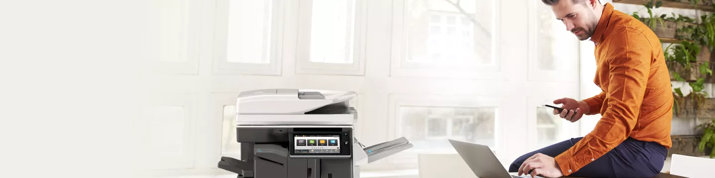 Man using laptop and smartphone next to a printer 